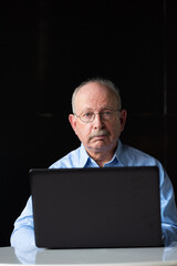 Grey haired senior man with mustache wearing eyeglasses and using laptop computer