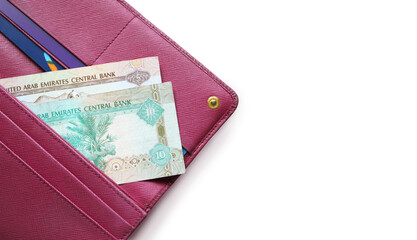 UAE dirham bills in a leather wallet. Fucsia red wallet, purse. Wood background. Banknotes. Money in cash. Stack of notes. Fan of bills. The currency of United Arab Emirates. AED