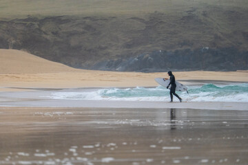 Fototapeta na wymiar Surfer returning from the sea on Eoropie beach on the Isle of Lewis, Scotland