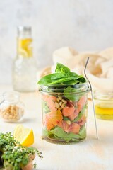 Healthy salad with spinach, red orange, salted fish and pine nuts in a glass jar on a light concrete background. Salad to go concept.
