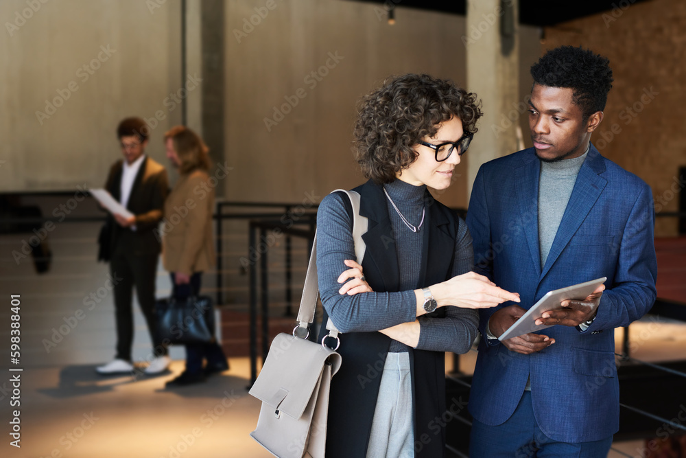 Poster Young businessman with tablet looking at female colleague pointing at screen while explaining online data during discussion of working points