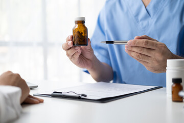 Close up of female doctor holding bottle of pills and explaining medication to patient in clinic.