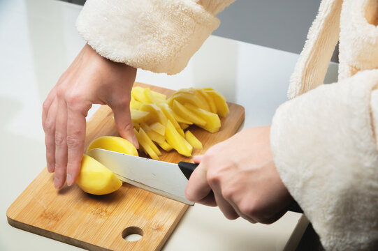 woman cuts potatoes on a wooden board. White background. Hands cut potatoes with kitchen pressure. food preparation