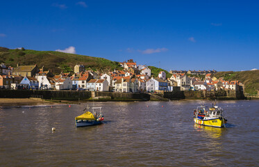 Obraz premium View across the harbour in Staithes at high tide.Two small fishing boats are moored in the middle of the harbour.