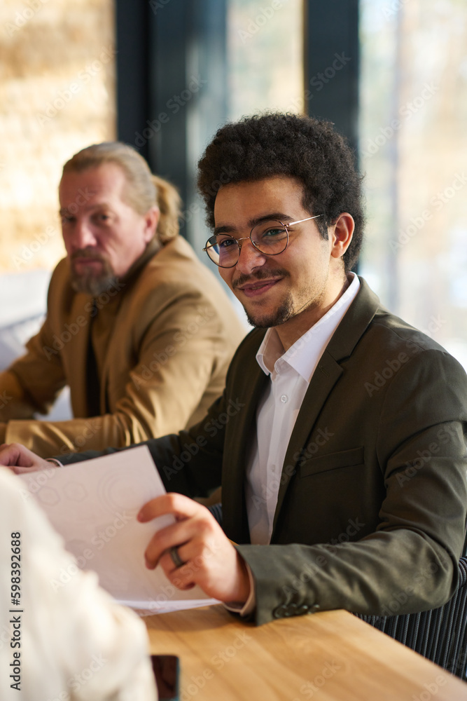 Poster Smiling male broker or economist with financial document in hand sitting in front of colleague during discussion of contract terms and conditions
