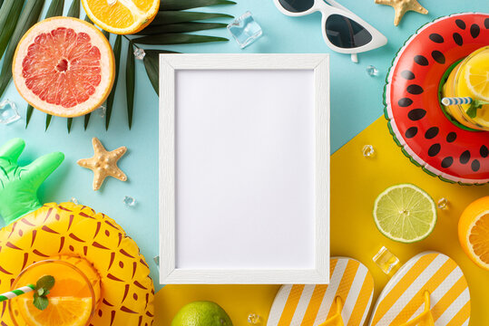 Summer refreshment vacation concept. Top view flat lay of pool float, cocktail glasses, palm leaves, citrus fruits, sunglasses and flip flops on blue and yellow background with empty frame for text