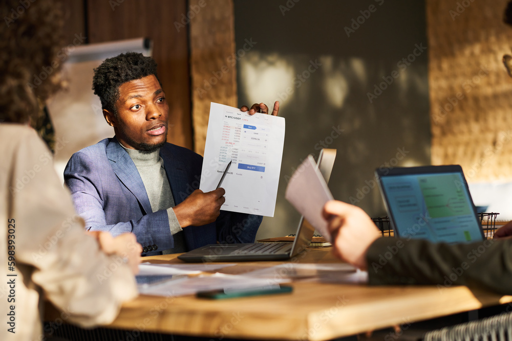 Poster young confident african american male broker pointing at document with financial data and explaining