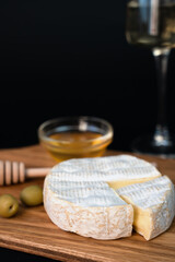 Camembert cheese, olives, honey and wineglass of white wine on a dark background. Close-up. Copy space. Selective focus.