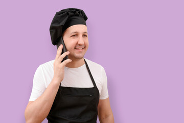 Smiling male chef using mobile phone on purple studio background. The concept of cooking