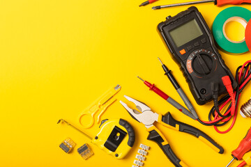 Electrician equipment on yellow background with copy space.Top view.Electrician tool set.Multimeter, tester,screwdrivers,cutters,duct tape,lamps,tape measure and wires.Flet lay. © Avocado_studio
