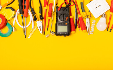 Electrician equipment on yellow background with copy space.Top view.Electrician tool set.Multimeter, tester,screwdrivers,cutters,duct tape,lamps,tape measure and wires.Flet lay.