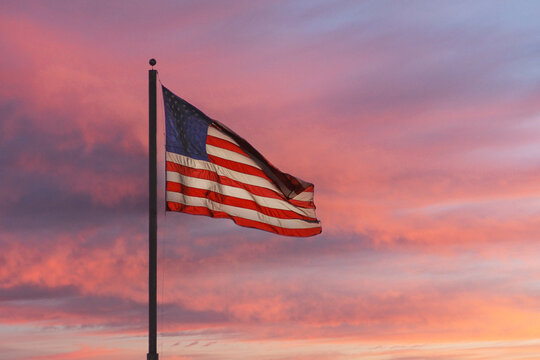 US flag waving with sunset colored clouds in background.