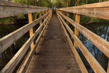 Fototapeta na wymiar Wooden footbridge over small river with early morning sun light leading nowhere