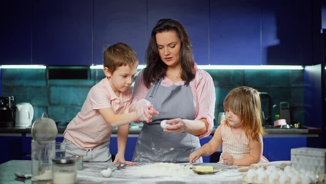 Caucasian son and daughter help their mother beat an egg into flour. The family prepares dough together in the kitchen at home. Cheerful joyful family together. High quality 4k footage Generative AI