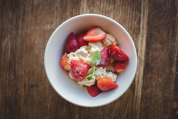 A bowl of strawberries and cream with leaves on a wooden table.