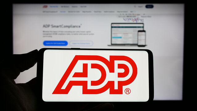Stuttgart, Germany - 04-26-2023: Person holding smartphone with logo of US company Automatic Data Processing Inc. (ADP) on screen in front of website. Focus on phone display.