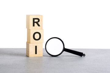 ROI - Return On Investment - text on wooden cube blocks and magnifying glass on grey table