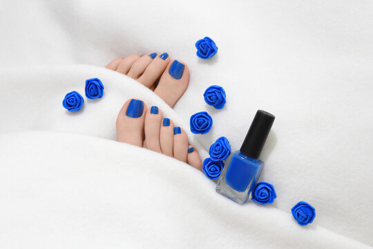 Close up of blue pedicured woman feet. Blue nails on white blanket. Feet are partially covered by white coverlet. Beauty concept.