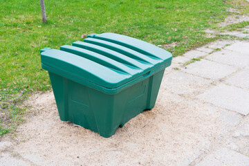 Green plastic waste container on sidewalk near grass