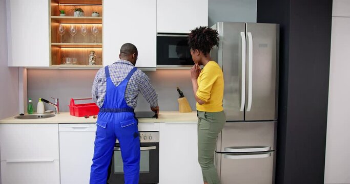 Woman Looking At Serviceman In Uniform Fixing Induction Stove