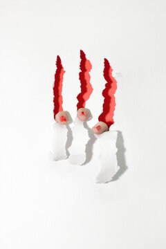 Red nails tearing the white paper from inside, showing red interior. Close up of female fingers, claws conceptual photo.
