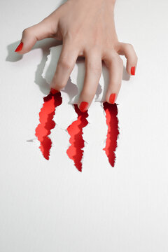 Claws conceptual photo. Female tear the white paper with her nails, showing red inside. Close up of hand.