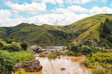 Fototapeta na wymiar Small brown river seen during trek to Pic Boby - Madagascar highest accessible peak in Andringitra national park, green hills with terraced fields background