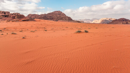Fototapeta na wymiar Rocky massifs, camp tens under - on red orange sand desert, bright cloudy sky in background, typical scenery in Wadi Rum, Jordan