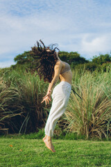 young latin woman with curls jumps in the nature barefoot, feeling of freedom. vertical photo