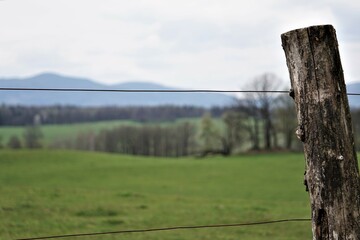 Ogrodzenie z drewna i drutu. Panorama roztaczająca się na góry w tle. Pastwisko dla bydła w tle. © Adam
