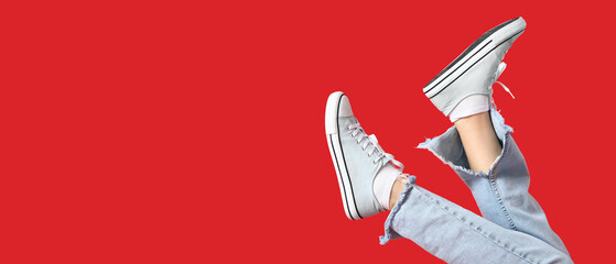 Legs of woman in stylish sneakers on red background with space for text - obrazy, fototapety, plakaty