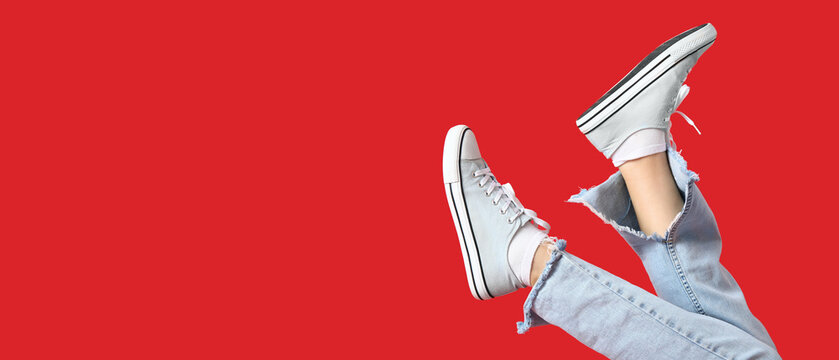 Legs of woman in stylish sneakers on red background with space for text
