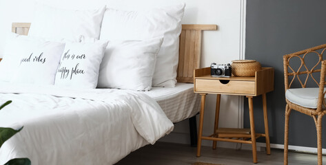 Fototapeta na wymiar Wooden nightstand with photo camera and wicker basket in light bedroom
