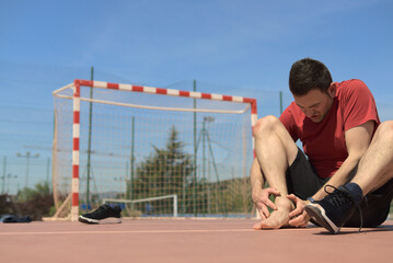 Athletic trainer is feeling his injuried articulation, put off shoe. The other leg is in front of him. Copy space colorful picture. Sports medicine and physical therapy concept. High quality photo
