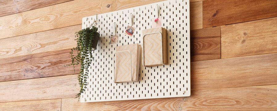 Hanging pegboard with notebooks, houseplant and photos on wooden wall in room