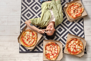 Happy young woman with boxes of tasty pizza showing victory gesture on floor, top view