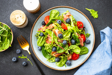 Green salad with fresh prosciutto, green leaves mix and tomatoes at dark table. Flat lay.