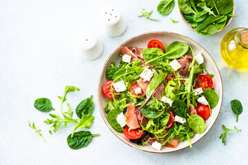 Healthy salad with green leaves, tomatoes and jamon. Vegetarian dish. Top view in craft plate.