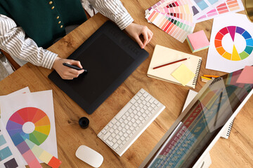 Female graphic designer working with tablet on table in office, top view