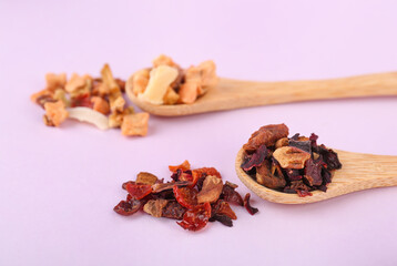 Wooden spoons with different dried fruit tea on pink background