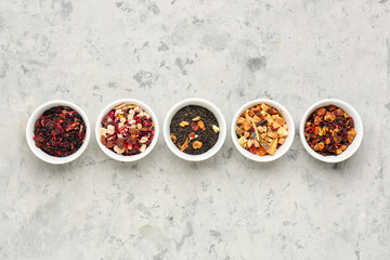 Bowls with different dried fruit tea on grey grunge table