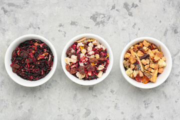 Bowls with different dried fruit tea on grey grunge table