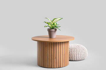 Wooden coffee table with houseplant and pouf on grey background