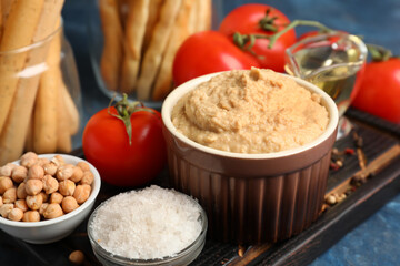Bowl of tasty hummus with ingredients on blue background