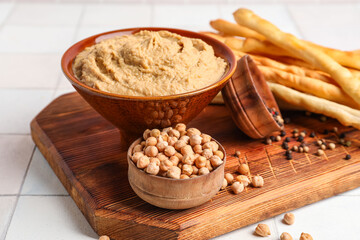 Bowl with tasty hummus on white tile background