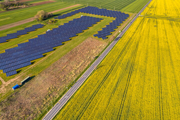 Aerial view of a solar panel farm on either side of a road and a yellow canola field on the other