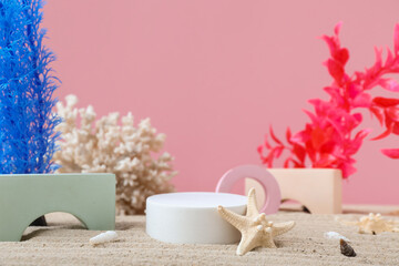 Decorative plaster podiums, coral, seaweed and starfish in sand on pink background
