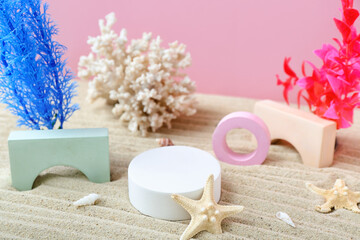 Decorative plaster podiums, coral, seaweed and starfishes in sand on pink background