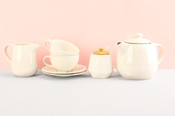 Teapot, sugar bowl, cups and pitcher on pink background