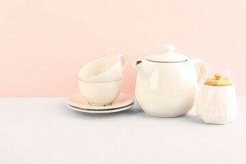 Fototapeta na wymiar Teapot, sugar bowl and cups on pink background